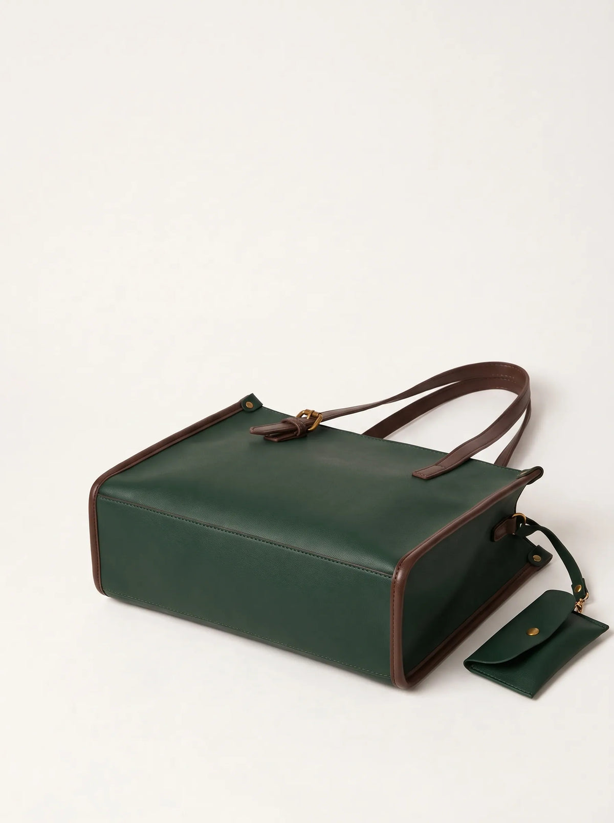 A dark green leather tote bag with brown trim and a matching small pouch, photographed on a clean off-white background.
